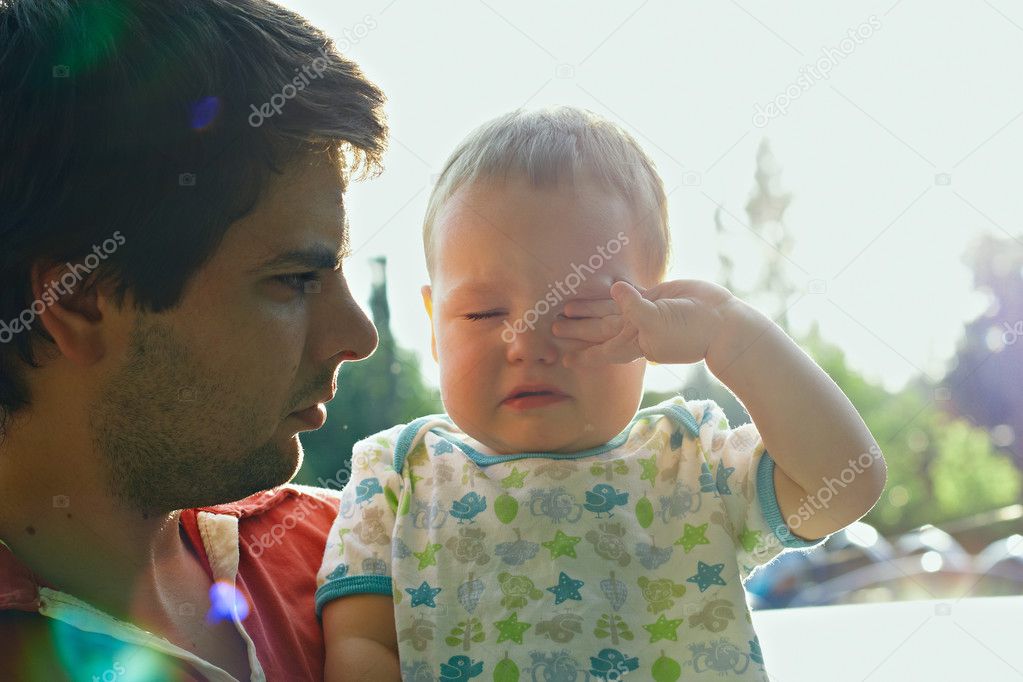 Dad is holding sweet crying son. back-lit with lens flare in the morning