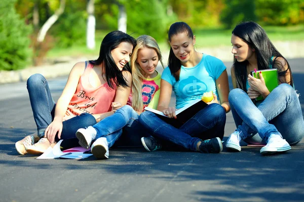 Four beautiful girls friends read books, sitting on the ground — Stock Photo, Image