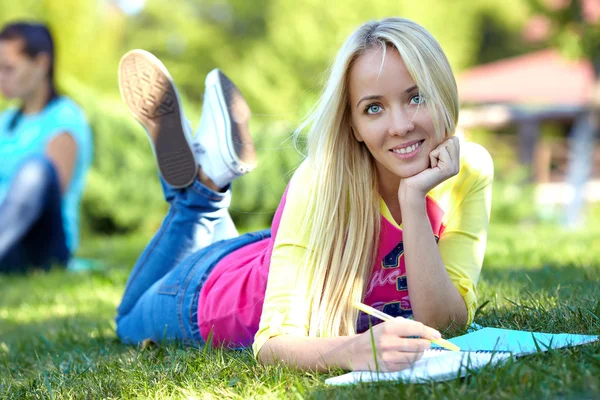 Hermosa estudiante se encuentra en el césped verde y aprende — Foto de Stock