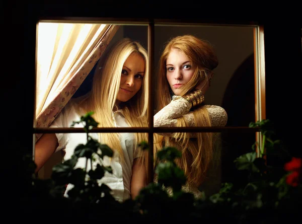 Two beautiful young women looking from window at night — Fotografie, imagine de stoc