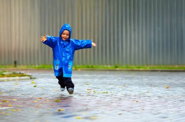 Happy baby boy running the street, rainy weather