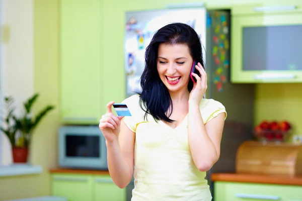 Mulher sorridente, chamando por telefone e holdind cartão de crédito, casa interior — Fotografia de Stock