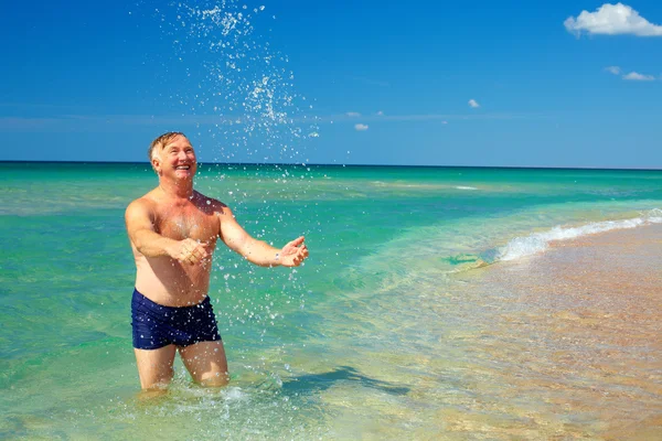 Счастливый взрослый мужчина плещется в воде на пляже — стоковое фото