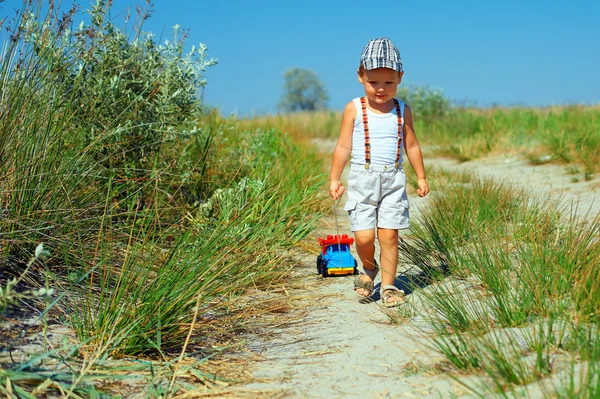 Carino bambino il sentiero del campo, trascinando auto giocattolo — Foto Stock
