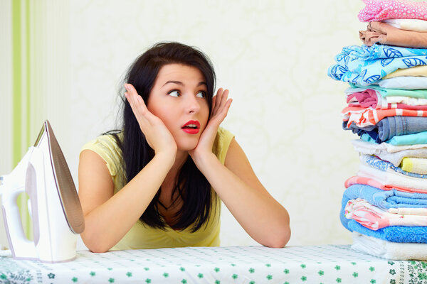 уставшая домохозяйка с огромной грудой гладильной прачечной
