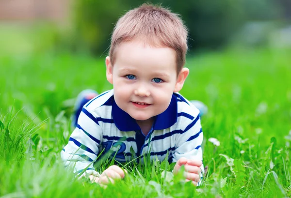 Happy baby boy lying on green grass in park Royalty Free Stock Images