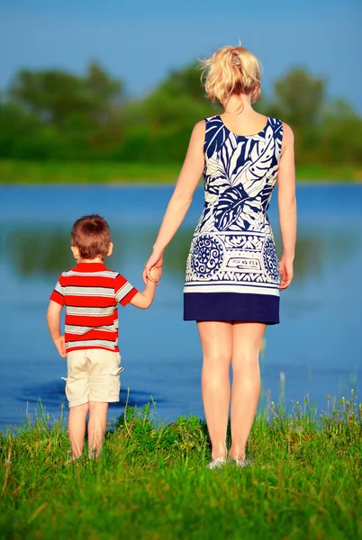 Young woman and baby boy holding hands on lake coast — Stock Photo, Image