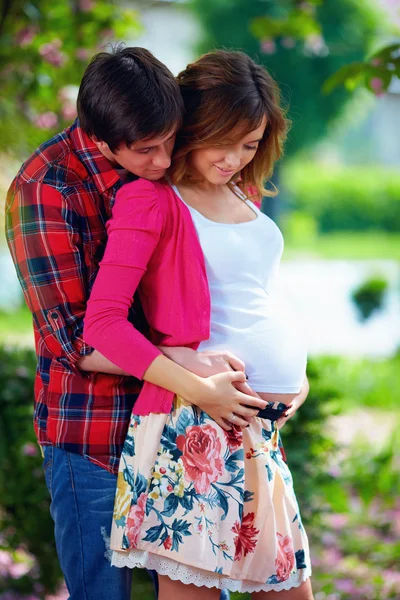 Молодая беременная пара в цветущем парке — стоковое фото