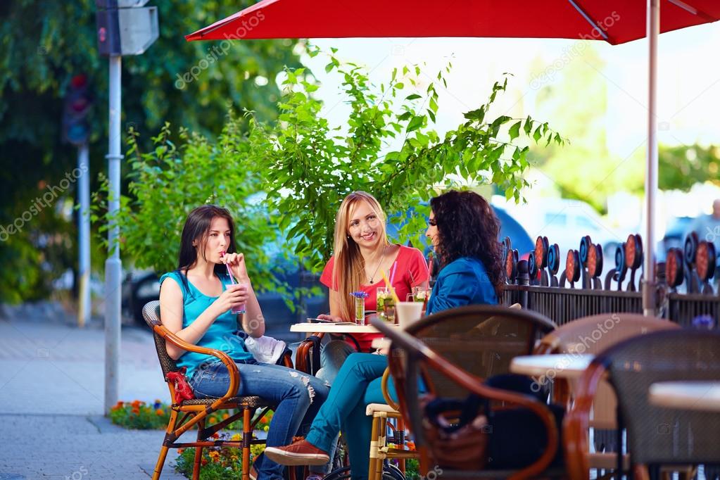 young female friends sitting on cafe terrace, urban outdoors