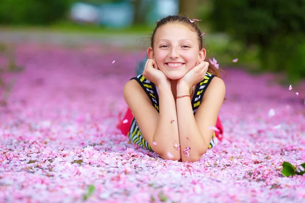 Gelukkig tienermeisje liggen in roze bloemblaadjes, lentetuin — Stockfoto