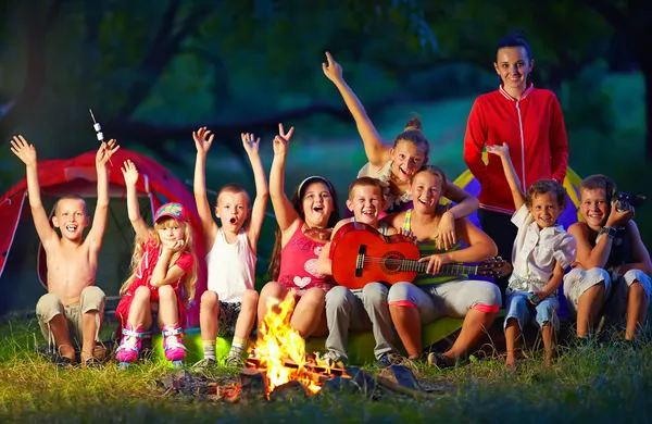 Crianças felizes cantando músicas ao redor fogo acampamento — Fotografia de Stock