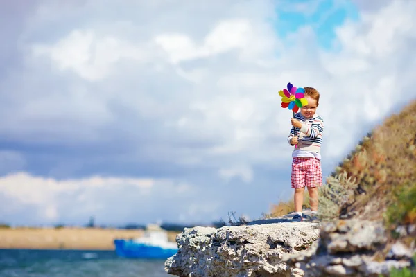 快乐的孩子与风车站立在靠近海边的悬崖上 — 图库照片