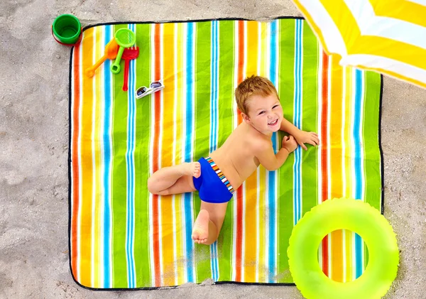 Feliz niño tomando el sol en la playa colorida — Foto de Stock