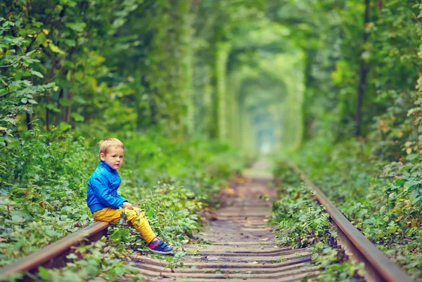 Милий хлопець сидить на рейках в зеленому тонелі — стокове фото