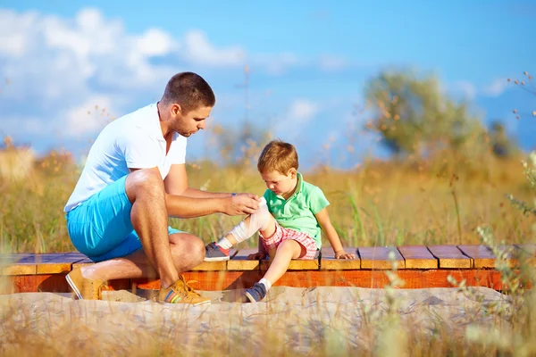 Padre vendaje lesionado pierna de niño — Foto de Stock