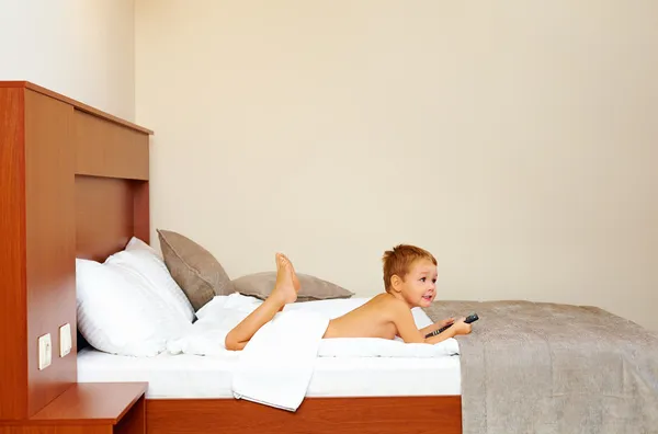 Niño feliz viendo la televisión en la habitación del hotel después de bañarse —  Fotos de Stock