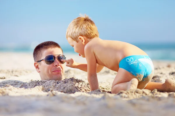 Far och son ha kul i sand på stranden — Stockfoto