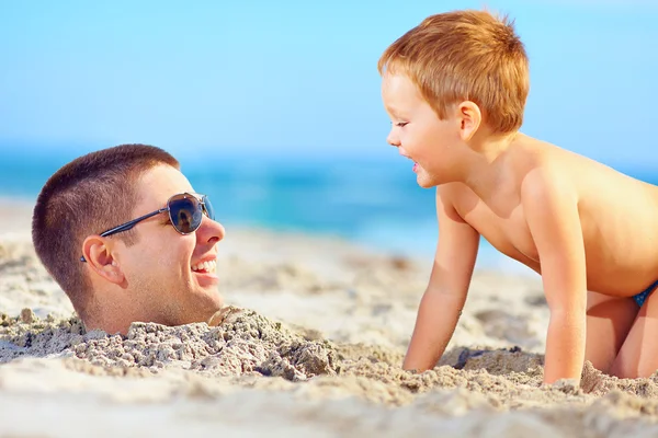 Pai e filho se divertindo na areia, rindo na praia — Fotografia de Stock