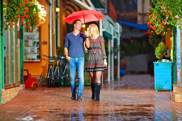 Happy couple walking under the rain on cozy colorful street — Stock Photo, Image