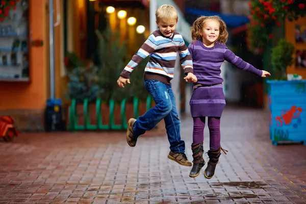 Niños felices saltando bajo la lluvia — Foto de Stock