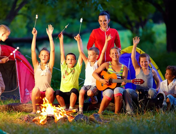 Niños felices cantando canciones alrededor del fuego del campamento —  Fotos de Stock