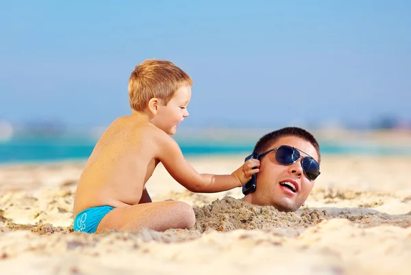 Happy kid helping father in sand talk on the mobile phone — Stock Photo, Image