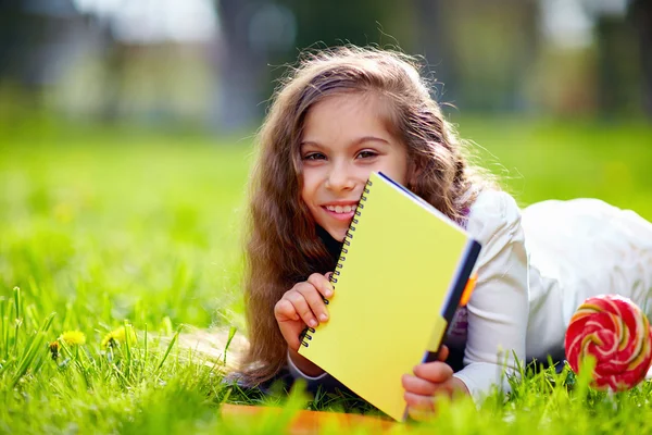 Beautiful young girl on green meadow with notebook — Stock Photo, Image