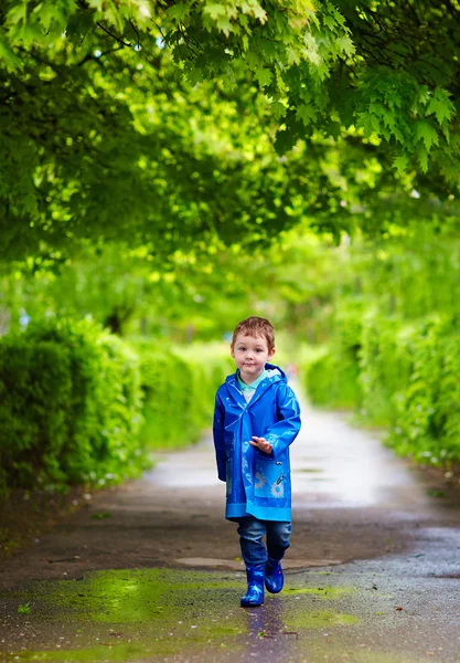 Mignon garçon marcher dans la rue des pluies — Photo