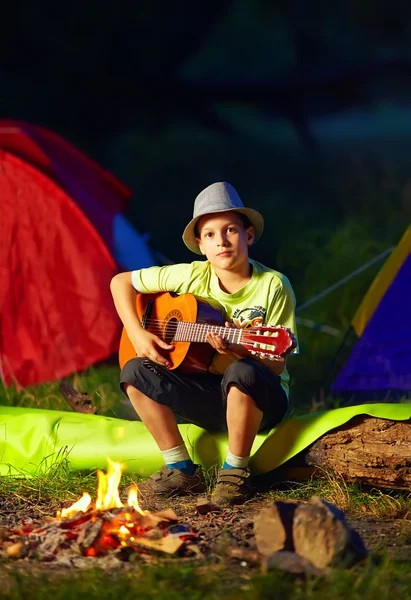 Menino tocando uma guitarra perto de fogueira, acampamento de verão — Fotografia de Stock