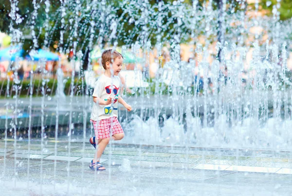 Ragazzo eccitato che corre tra il flusso d'acqua nel parco della città — Foto Stock