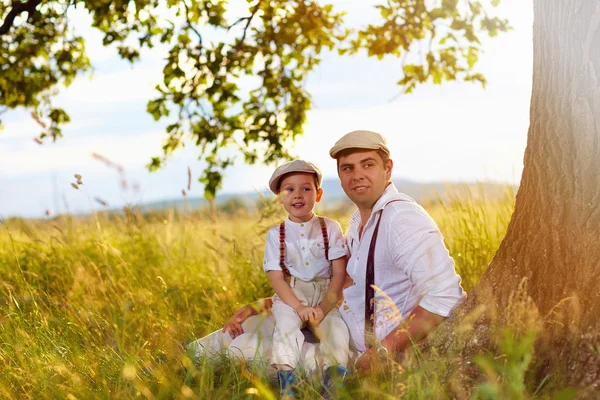 Father and son sitting under an old oak tree — Stock Photo, Image