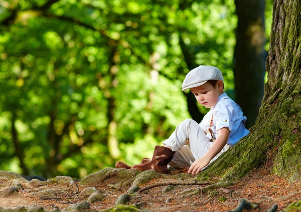 Süsser Boy sitzen unter einem alten Baum im Wald — Stockfoto