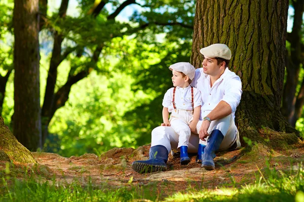 Father and son sitting under an old tree in forest — Stock Photo, Image