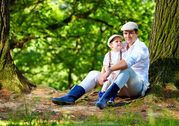 Father and son sitting under an old tree in forest — Stock Photo, Image