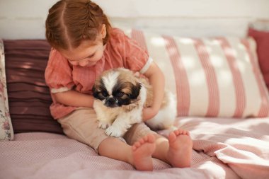 Evdeki yazlık terasta yavru köpeğe sarılan tatlı bir kız.