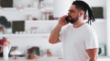 Rastalı genç bir adam evde telefonla konuşuyor.