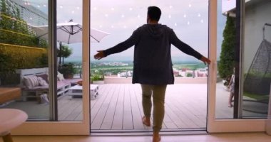 Adam sürgülü kapılar açıyor, bir vadideki güzel şehir manzaralı terasa çıkıyor.