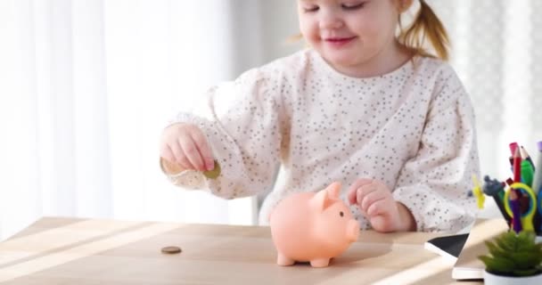 幼い頃から子供を救うこと 幸せな幼児の赤ん坊の女の子は貯金箱に硬貨を落とす あなたの子供にお金箱で予算を計画するように教える — ストック動画