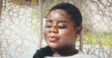 Göz kamaştırıcı genç kadın güneşli bir günde sallanan sandalyede dinleniyor