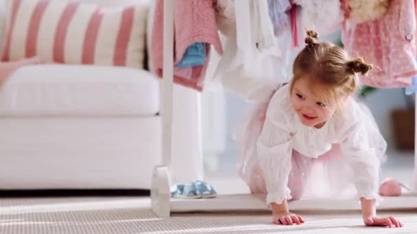 かわいい赤ちゃんが楽しそうに服の下を這って家の日当たりの良い部屋に立つ — ストック動画