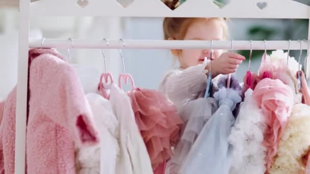 快乐的小女孩把衣服挂在衣架上 站在托儿所里 — 图库视频影像