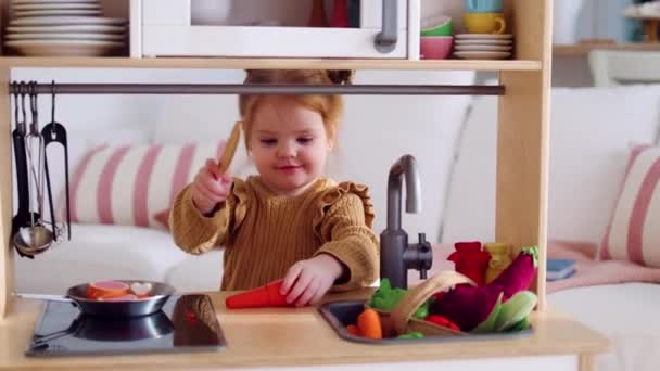 阳光明媚的日子 可爱的小女孩在育婴室切木制玩具胡萝卜 — 图库视频影像
