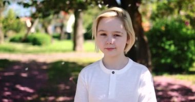 Güneşli bir günde bahar bahçesinde çiçeklerin altında mutlu bir sarışın çocuk.