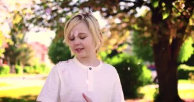 Güneşli bir günde bahar bahçesinde çiçeklerin altında mutlu bir sarışın çocuk.