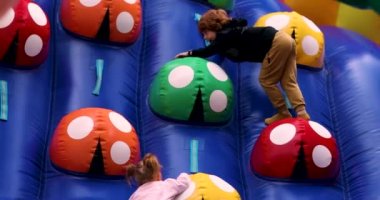 Çocuklar şişme parkta eğleniyor, lunaparktaki renkli duvara tırmanıyor.