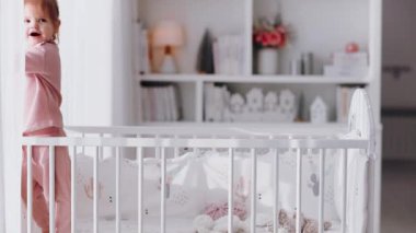 Evdeki bebek odasındaki beşikte dururken perdeyle oynayan küçük kız.