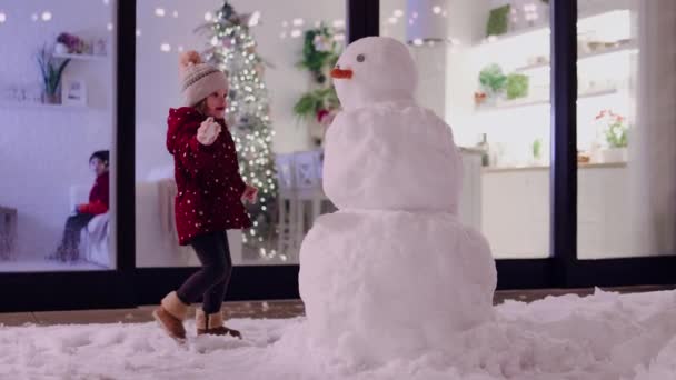 小女孩很开心 在冬夜和雪人在院子里玩耍 — 图库视频影像