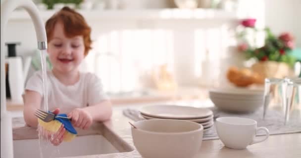 陽気な子供は水道水の下でフォークや皿を洗い — ストック動画
