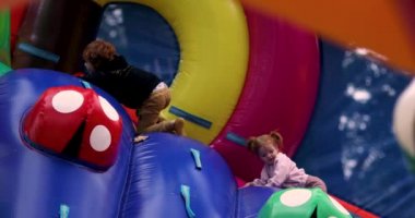 Çocuklar şişme parkta eğleniyor, lunaparktaki renkli duvara tırmanıyor.