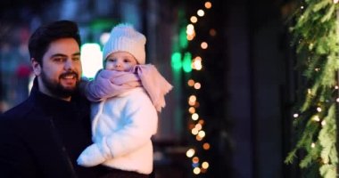 Mutlu baba ve bebek Noel alışverişi yapıyor, Winter City caddesinde yürüyor.